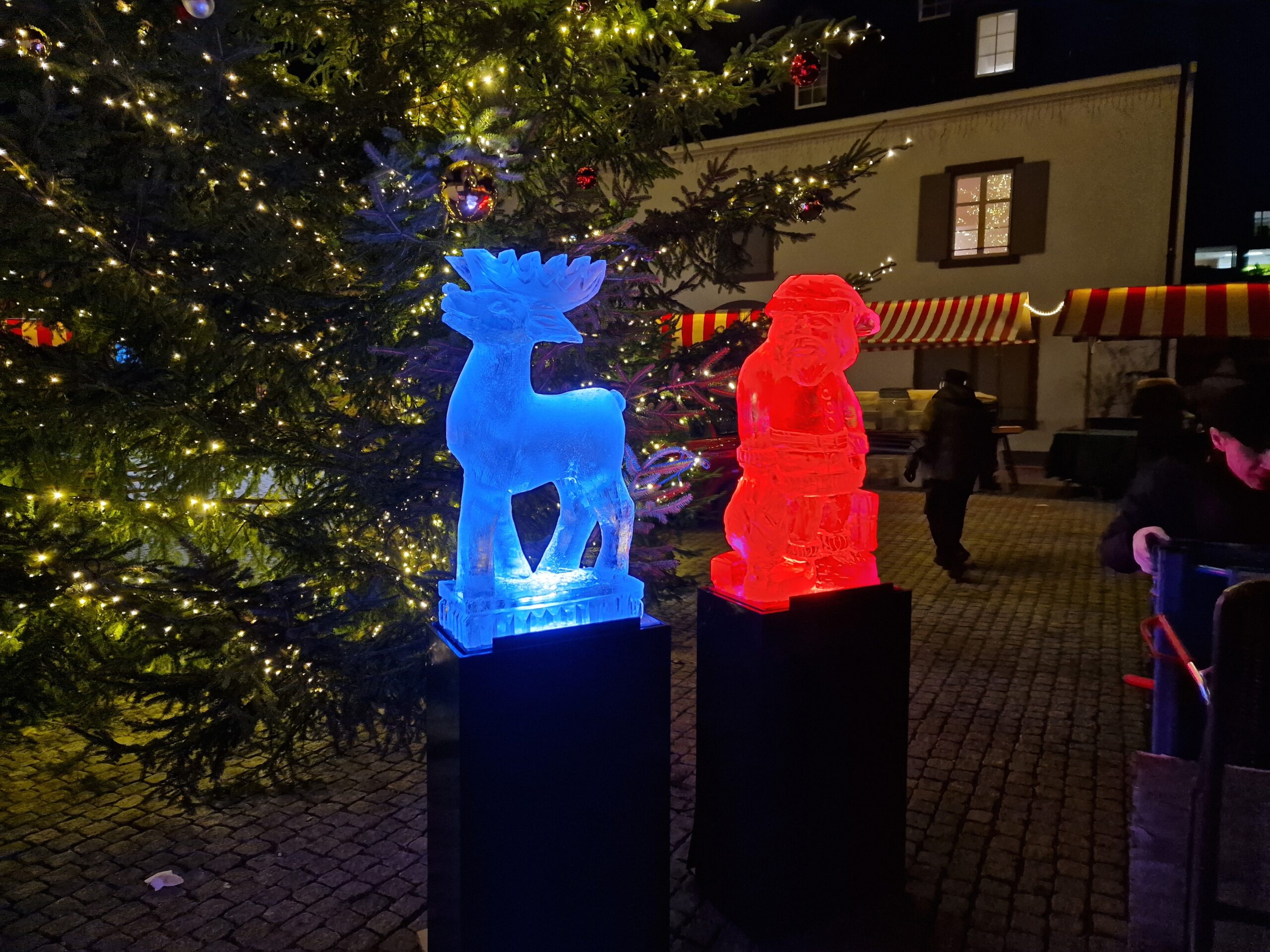blau beleuchtetes Rehntier und rot beleuchteter Samichlaus aus Eis am Weihnachtsmarkt 2024